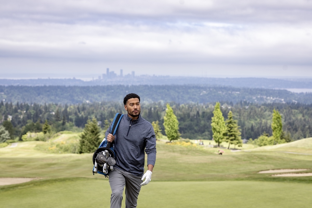 Man wearing a Cutter & Buck Adapt Stripe Q zip pullover while walking with golf bag